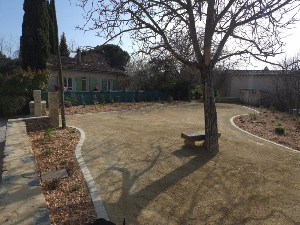 Cour en gravier stabilisé avec massifs paillés et piliers en pierre aménagée par Gonsalves Paysages