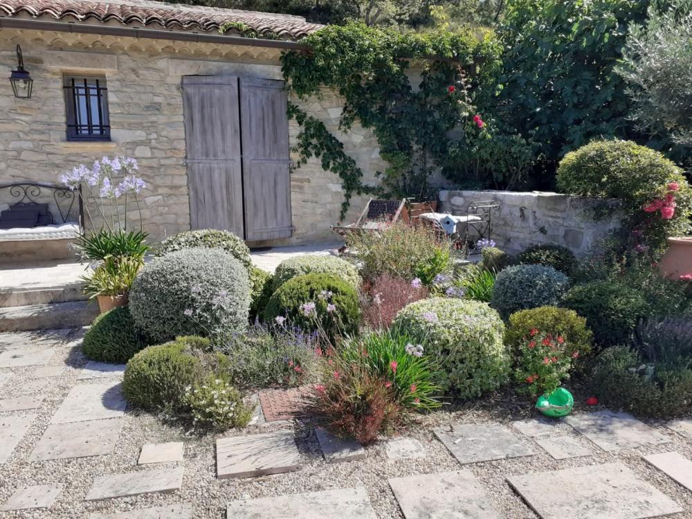 Massif paysager méditerranéen avec arbustes en boules et agapanthes devant un mas en pierre